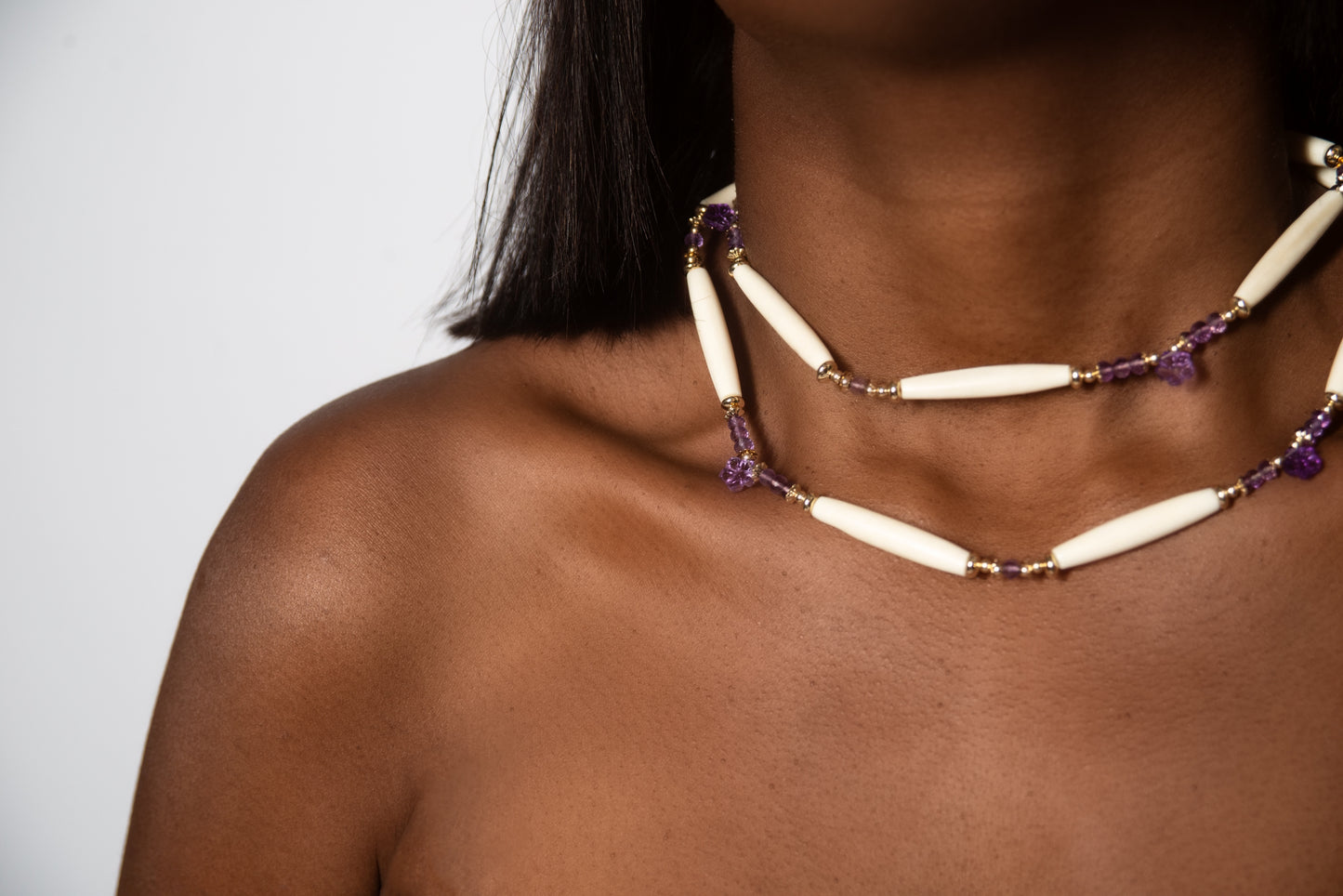 A woman wearing the Ilium Wing Enthrone necklace with purple and white beads that symbolizes tranquility and spirituality.