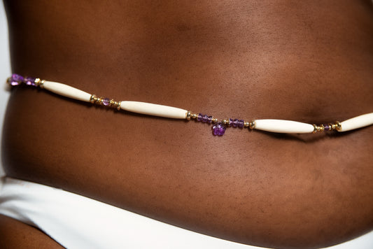A woman in a bikini with an Enthrone beaded belt by Ilium Wing engages in meditation and visualization.