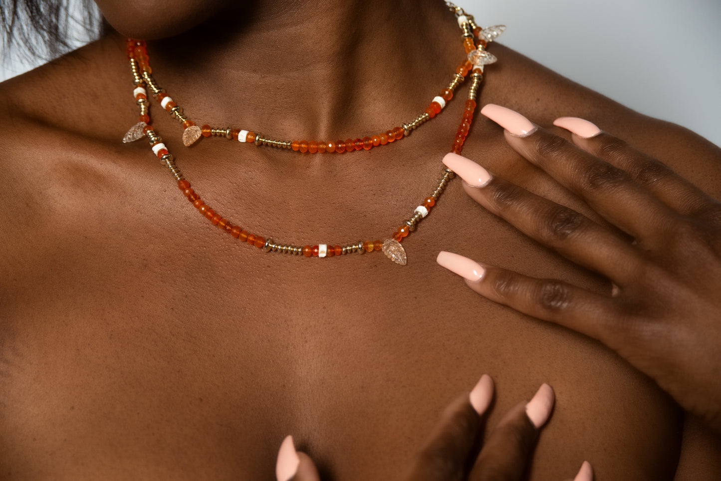 A woman wearing the "Awaken" necklace from the brand "Ilium Wing" with vibrant orange and shimmering gold beads, evoking the energy of the Sacral Chakra and igniting a playful fire within.