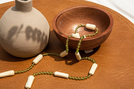 A Caravan necklace with green beads and a vase on a brown table by Ilium Wing.